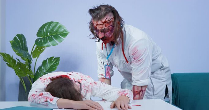 Furious zombie in doctor coat attacks and eats dead young woman. Hungry spooky man with mustache and covered with blood eats flesh of nurse corpse