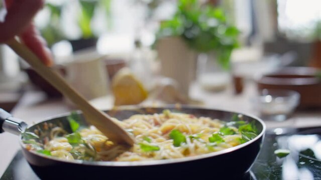 Close up view of hand stirring hot spaghetti in skillet with wooden spoon