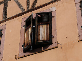 Zur Mittagszeit halb geschlossene alte Fensterläden an einem alten Fachwerkhaus im Elsass