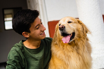 latino teenager laughing with his golden retriever dog sitting in the driveway