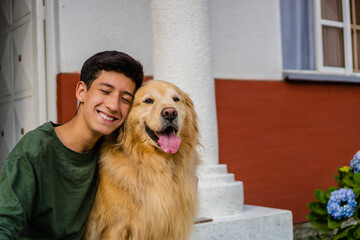latin teenager hugging his golden retriever dog sitting in the driveway. copy space
