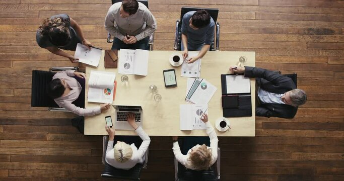 a group of businesspeople having a meeting in a modern office. A group of businesspeople brainstorming in a meeting in a boardroom, reading paperwork from above. Colleagues in marketing meeting