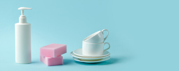 White plastic bottle for liquid soap or dishwashing gel, pink sponges and white cups on blue background, kitchenware, house cleaning service concept, copy space, banner, flyer, mockup