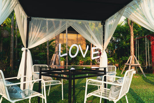Empty dining table with chairs in the green garden area, decoration design with natural background in summer, feeling relax with flower, plant. Love text sign.