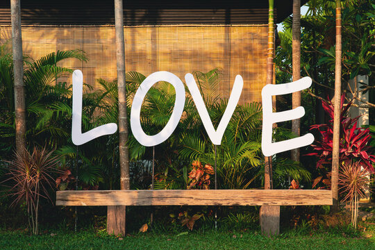Long vintage wooden chair with nature background in summer, feeling relax with flower, plant and love text sign.