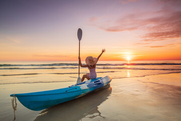 Young lady tourist and canoe on the beach with sunset on the sea at Phuket province, Thailand.