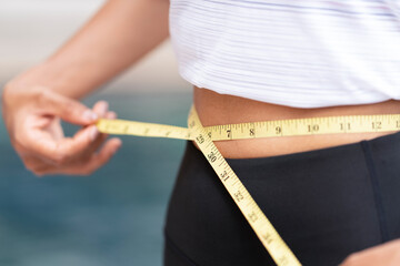 Closed up fit woman using yellow waistline to measure her slim waist and torso after controlling her nutrition, weight loss during diet and exercise.