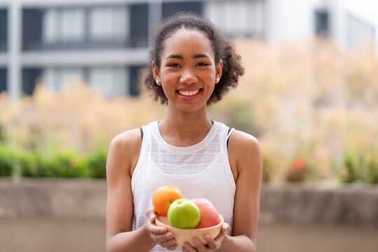 Young black woman holding low sugar fruits in the wooden bowl to diet and body slim fit including getting vitamin c, fiber from natural fruits after finish outdoor workout at home, raw food snack