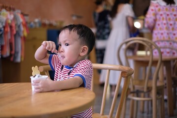 Little Asian kid boy eating ice cream in indoor cafe or restaurant.