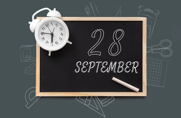 september 28. 28th day of month, calendar date. Blackboard with piece of chalk and white alarm clock on green background. Concept of day of year, time planner, autumn month