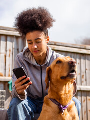 Girl with dog in backyard, checking smartphone