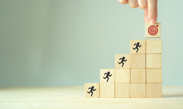 Common goal success concept. Teamwork rises up stairs to goal and achieve successful business. Initiation for planning to reach target. Darts target aim icon on wooden cubes with grey background.
