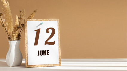 june 12. 12th day of month, calendar date.White vase with dead wood next to cork board with numbers. White-beige background with striped shadow. Concept of day of year, time planner, summer month