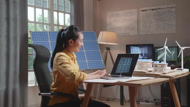 Side View Of Asian Woman Shaking Her Head While Looking Solar Cell On The Laptop Next To A Small House With Solar Panel And Wind Power

