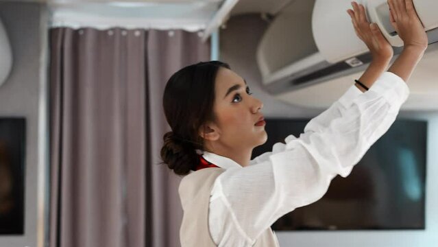 Asian beautiful female flight attendants closing overhead cabinet luggage compartment for checking safety of passenger before airplane take off and Group of people in airplane. Airline concept.