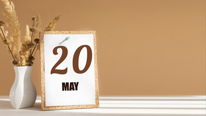 may 20. 20th day of month, calendar date.White vase with dead wood next to cork board with numbers. White-beige background with striped shadow. Concept of day of year, time planner, spring month