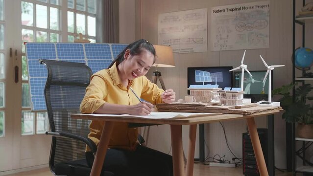Asian Woman Sketch House With Solar Panel On The Blueprint While Holding It In Hand

