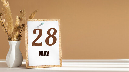 may 28. 28th day of month, calendar date.White vase with dead wood next to cork board with numbers. White-beige background with striped shadow. Concept of day of year, time planner, spring month