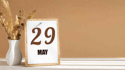 may 29. 29th day of month, calendar date.White vase with dead wood next to cork board with numbers. White-beige background with striped shadow. Concept of day of year, time planner, spring month