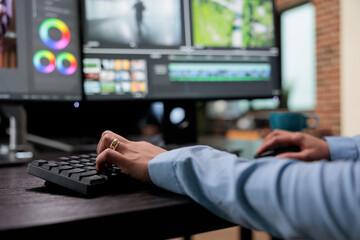 Close up shot of digital video editor sitting at multi monitor workstation desk while working on movie footage. Creative post production house videographer improving film frames visual quality. - obrazy, fototapety, plakaty