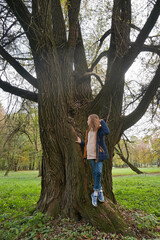 Dreamily schoolgirl in park near giant willow tree in early autumn
