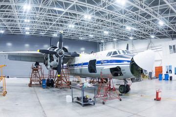 White transport turboprop airplane in the hangar. Aircraft under maintenance. Checking mechanical...