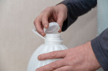 A man opens a white bottle of drinking water. The man's hand holds the cork on top of the plastic bottle.