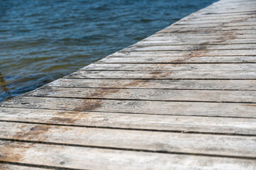 Fototapeta premium The weathered planks of the pier against the water. The old planks of the small pier on the shore. Close-up. Selective focus.