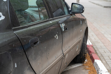 A sedan with through holes from shrapnel stands in a parking lot. The shelled car. The war in...