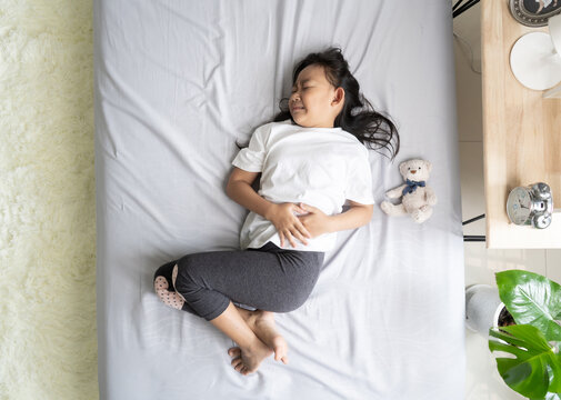 Top view Asian child little girl in her bed has a stomachache, healthy idea concept