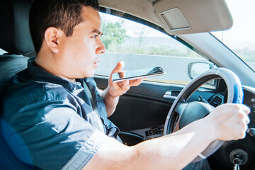 Man in his car sending voice notes with his cell phone, Side view of a young man sitting inside the...