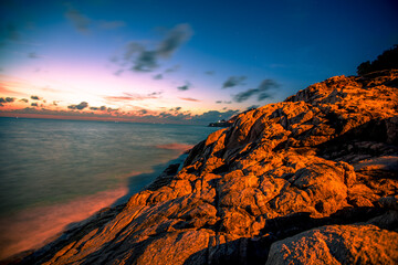 Blurred nature background of the morning sun by the sea, a beautiful golden light, among the trees, rocks and local fishing boats, the beauty of nature during the day.