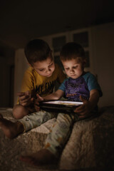 Cute little boys using tablet playing video games, sitting on bed at home