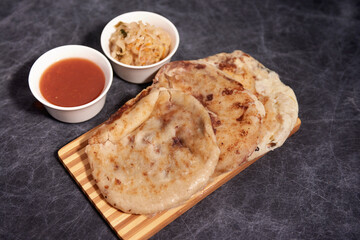 Pupusas on a wooden board with curtido and sauce over a black marble background
