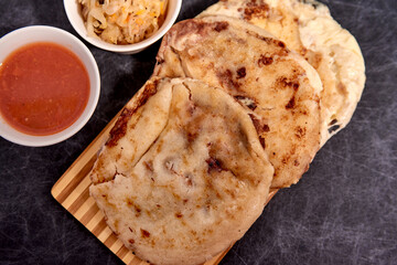Close up Pupusas on a wooden board with curtido and sauce over a black marble background