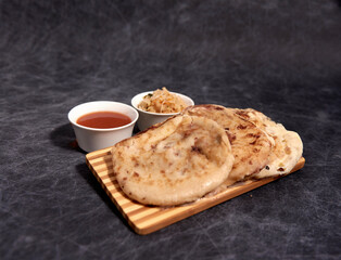 Pupusas on a wooden board with curtido and sauce over a black marble background - obrazy, fototapety, plakaty