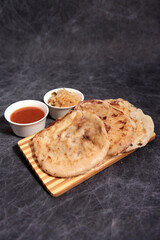 Pupusas on a wooden board with curtido and sauce over a black marble background
