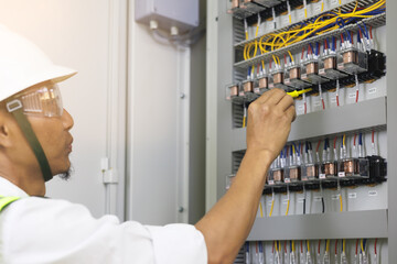 A male electrician works in a control panel with electrical connections connecting devices with a...