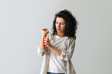 Young woman with allergy scratching herself on grey background