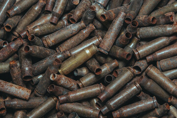 
A lot of used old, rusty brass cartridge cases from the machine. Empty carbine or rifle cartridges. Background of brass ammunition cartridges to illustrate armed conflict, war or shooting.