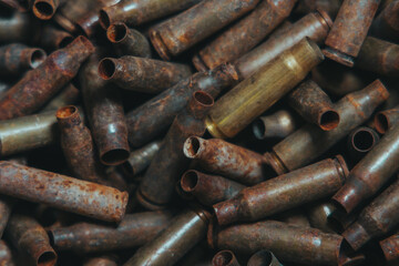 
A lot of used old, rusty brass cartridge cases from the machine. Empty carbine or rifle cartridges. Background of brass ammunition cartridges to illustrate armed conflict, war or shooting.