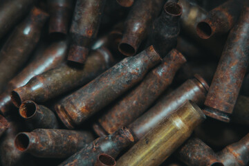 
A lot of used old, rusty brass cartridge cases from the machine. Empty carbine or rifle cartridges. Background of brass ammunition cartridges to illustrate armed conflict, war or shooting.