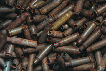 
A lot of used old, rusty brass cartridge cases from the machine. Empty carbine or rifle cartridges. Background of brass ammunition cartridges to illustrate armed conflict, war or shooting.