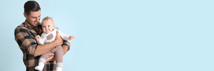 Happy man holding cute baby on light blue background with space for text