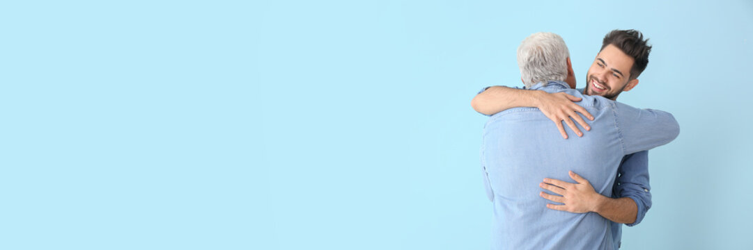 Happy young man hugging his father on light blue background with space for text