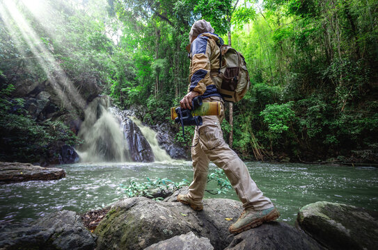 Male hiker with backpack and binoculars explores new waterfall in forest