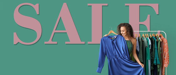 Beautiful African-American girl near rack with clothes and word SALE on green background