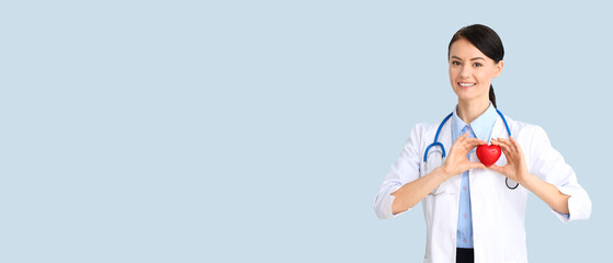 Female cardiologist holding red heart on light blue background with space for text
