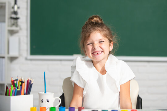 Cute little preschooler child girl drawing at school. Child girl painting on elementary school. Funny school girl face.