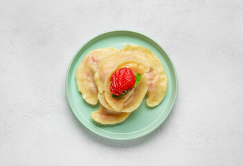 Plate with strawberry dumplings on light background
